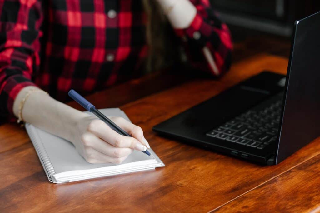 Cropped image of a woman writing in the notebook to compare quotes from multiple man and van companies